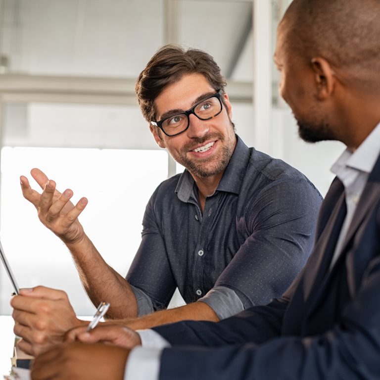Young smiling businessman wearing eyeglasses and discussing work with senior manager. Two office colleagues in meeting room brainstorming on creative ideas. Happy business man in office working with african leader.